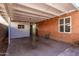 Covered patio with a red brick wall, concrete floor, and metal gate accessing backyard space at 6811 N 11Th Ave, Phoenix, AZ 85013