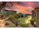 Sunset view of backyard oasis with putting green, pool, and waterfall feature at 37181 N 103Rd St, Scottsdale, AZ 85262
