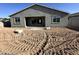 Backyard view of a new gray single-story home showcasing an unfinished yard and covered patio at 5510 W Paseo Way, Laveen, AZ 85339