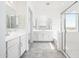 Open bathroom with double vanities, tub, and glass shower, featuring neutral tile flooring at 25505 W Brookhart Way, Wittmann, AZ 85361
