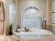 Luxurious bathroom with a soaking tub and arched window with shutters at 13462 E Wethersfield Rd, Scottsdale, AZ 85259