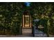 Exterior entrance featuring lush greenery, a decorative metal door, and warm lighting at 6529 E Camino De Los Ranchos St, Scottsdale, AZ 85254