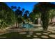 Backyard swimming pool and adjacent fire pit area are framed by mature trees, creating a peaceful nighttime oasis at 6529 E Camino De Los Ranchos St, Scottsdale, AZ 85254