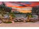 Backyard with a rock waterfall feature, desert landscaping, mature trees, and wrought iron fence under a sunset sky at 28247 N 128Th Dr, Peoria, AZ 85383