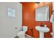 Stylish bathroom with orange accent wall, pedestal sink, and modern fixtures at 35298 W San Ildefanso Ave, Maricopa, AZ 85138