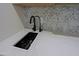 Close-up of stainless steel sink with black faucet and light-floral tile backsplash at 18 W Kaler Dr, Phoenix, AZ 85021