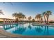 Beautiful community pool at dusk, featuring palm trees, lounge chairs, and tranquil water at 41929 W Springtime Rd, Maricopa, AZ 85138