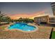 Sparkling swimming pool with a patio and desert landscaping at sunset at 22717 W Sierra Ridge Way, Wittmann, AZ 85361