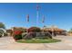 Community entrance with a decorative stone sign, manicured landscaping, and flags against a clear blue sky at 3254 N Ladera Cir, Mesa, AZ 85207