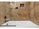 Close-up of a white bathtub with a glass partition and tiled walls with built-in shelves in the shower area at 13248 N 12Th Pl, Phoenix, AZ 85022