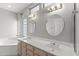 Bathroom with dual sinks, decorative mirrors, vanity with storage, and glass block window at 15704 W Sentinel Dr, Sun City West, AZ 85375