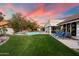 Backyard with lush lawn, pool, shade trees and comfortable lounge chairs on the rear patio at sunset at 9504 E Sunnyside Dr, Scottsdale, AZ 85260