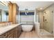 Bright bathroom features a soaking tub under a window, walk-in shower and wooden cabinets at 9504 E Sunnyside Dr, Scottsdale, AZ 85260