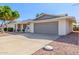 Single-level home featuring a two-car garage, manicured landscaping, and mature trees at 9827 W Lindgren Ave, Sun City, AZ 85373