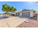 Single-level home featuring a two-car garage, manicured landscaping, and mature trees at 9827 W Lindgren Ave, Sun City, AZ 85373