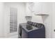 Bright laundry room featuring a blue washer and dryer set, subway tile backsplash, plantation shutters, and white cabinets at 8708 E San Lucas Dr, Scottsdale, AZ 85258