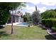 A backyard featuring a pool, mature trees, green lawn, patio, and a lush garden at 4119 E Glencove St, Mesa, AZ 85205