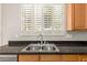 Close-up of the kitchen sink, granite countertop, wooden cabinets, and window with plantation shutters at 4286 E Buckboard Rd, Gilbert, AZ 85297