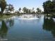 Scenic view of a pristine pond with a central water fountain, surrounded by lush greenery and mature trees at 9714 E Cochise Pl, Sun Lakes, AZ 85248