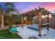 Outdoor fireplace under a pergola, set on stone tiles with a lush green hedge and tree in the background at 3005 E Valencia Dr, Phoenix, AZ 85042