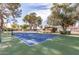Well-maintained blue and green tennis court with net, surrounded by trees and fencing at 131 N Higley Rd # 215, Mesa, AZ 85205