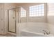 Well-lit bathroom featuring a tub with glass shower doors and a tiled surround with accent glass blocks at 18060 W Rimrock St, Surprise, AZ 85388