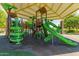 An inclusive playground with green slides and interactive panels under a protective shade structure at 42735 W Bravo Dr, Maricopa, AZ 85138