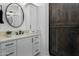 Modern bathroom vanity with white cabinets, quartz countertop, round mirror, and stylish barn door at 9412 E Hidden Spur Trl, Scottsdale, AZ 85255