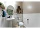 A compact half bathroom featuring a pedestal sink, toilet, a decorative mirror, and shelving at 18118 W Golden Ln, Waddell, AZ 85355