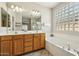 Bright bathroom features a double vanity, large mirror, soaking tub, and glass block window at 20477 N 91St Dr, Peoria, AZ 85382