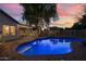 Backyard pool illuminated at dusk, reflecting the vibrant sky, surrounded by a brick patio and white fencing at 928 S San Joaquin Ct, Gilbert, AZ 85296