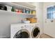 Well-organized laundry room with stacked washer and dryer, storage shelves, and access to the backyard at 13633 N 111Th Ave, Sun City, AZ 85351