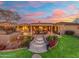 Beautiful outdoor living space with a fire pit, lush green lawn, and steps leading to a covered patio with sunset view at 27606 N 61St Pl, Scottsdale, AZ 85266