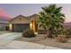 Charming single-story home featuring a dark garage door, desert landscaping and warm exterior lighting at 41954 W Plata St, Maricopa, AZ 85138