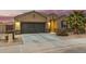 Charming single-story home featuring a dark garage door, desert landscaping and warm exterior lighting at 41954 W Plata St, Maricopa, AZ 85138