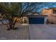 Inviting single-story home with gravel landscaping, a blue garage door, and mature desert tree at 10594 E Wallflower Ln, Florence, AZ 85132