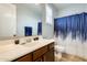 Well-lit bathroom featuring a vanity with dark wood cabinets and a blue patterned shower curtain at 18256 W Carol Ave, Waddell, AZ 85355