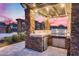 Outdoor kitchen with stainless steel grill, mini-fridge, and stone countertops, ideal for outdoor entertaining as the sun sets at 28826 N 67Th Dr, Peoria, AZ 85383