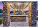 Outdoor kitchen with stone accents and bar seating, creating a cozy space for dining and entertaining with lush landscape at 28826 N 67Th Dr, Peoria, AZ 85383