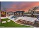 Luxury pool area featuring a pergola with stone pillars, manicured lawn, and an outdoor kitchen at sunset at 28826 N 67Th Dr, Peoria, AZ 85383