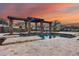 Luxury swimming pool featuring a pergola with stone pillars, and waterfall features at sunset at 28826 N 67Th Dr, Peoria, AZ 85383