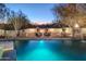 Inviting pool with a tranquil waterfall feature and cozy outdoor fireplace seating area at dusk at 35530 N Canyon Crossings Dr, Carefree, AZ 85377