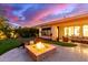 Inviting backyard featuring a stone fire pit, putting green, and elegant outdoor seating under a colorful sunset sky at 4675 S Bandit Rd, Gilbert, AZ 85297