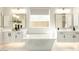 A bathroom with a tub, white cabinets, two mirrors, and a window at 12245 E Clinton St, Scottsdale, AZ 85259