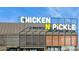 Modern Chicken N Pickle restaurant with a metal facade, geometric design elements, and prominent signage against a blue sky at 8516 W Peppertree Ln, Glendale, AZ 85305