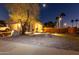 Home exterior featuring desert landscaping, mature trees, a tiered fountain, and exterior lighting for evening ambiance at 11197 W Coronado Rd, Avondale, AZ 85392