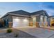 Modern home showcasing a large two-car garage and a covered entrance with stone accents and a well-lit driveway at 23282 S 229Th Pl, Queen Creek, AZ 85142