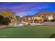 Expansive backyard with a putting green, lounge seating, and shimmering blue pool at twilight at 6626 E Oberlin Way, Scottsdale, AZ 85266