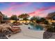 Backyard pool with lounge chairs, manicured shrubbery, rock waterfall, and a beautiful sunset sky at 6626 E Oberlin Way, Scottsdale, AZ 85266