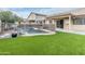 Backyard pool with a safety fence, artificial grass, and waterfall feature with lush landscaping at 9001 W Lone Cactus Dr, Peoria, AZ 85382